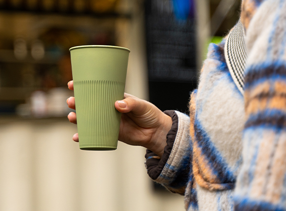 Woman carrying green reusable takeaway coffee cup